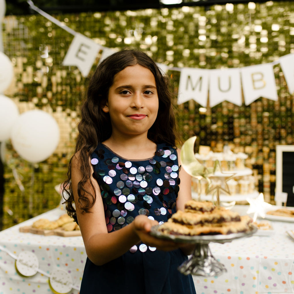 Young girl holding a cake stand with a decorated backdrop