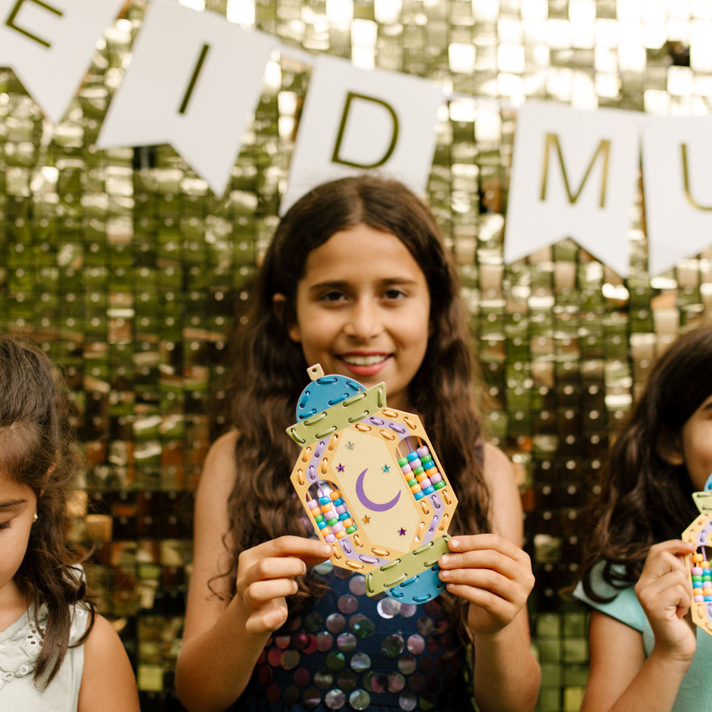 Three children holding decorated lantern with 'EID MUBARAK' banner in the background