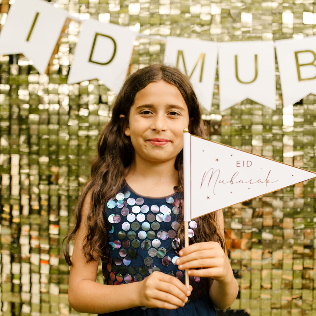 Young girl holding a 'Eid Mubarak' flag with a glittery gold backdrop
